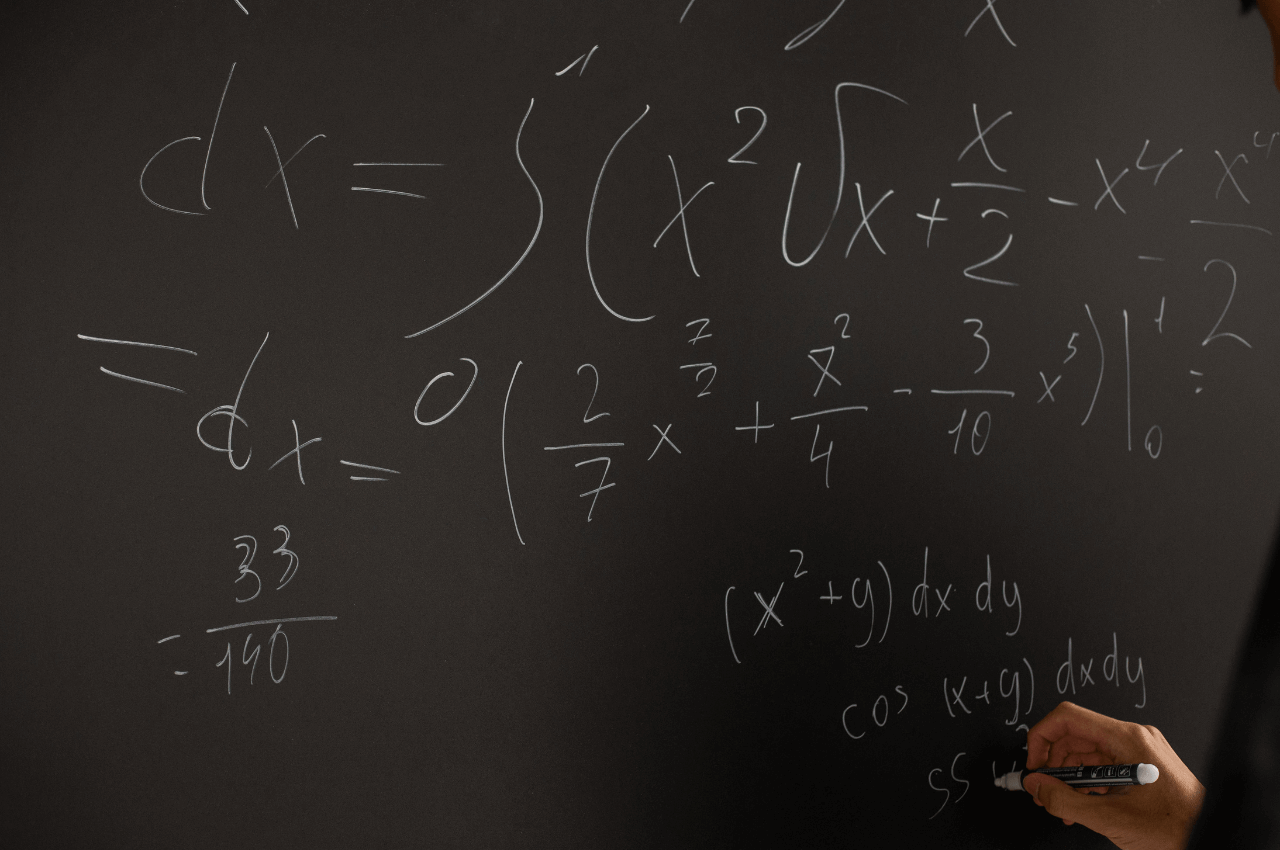 A picture of a person writing an equation on a black board.